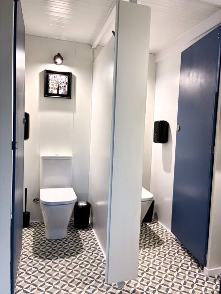 Baño con inodoro, dispensador de jabón y paredes de color blanco y azul. Suelo de azulejos decorativos.